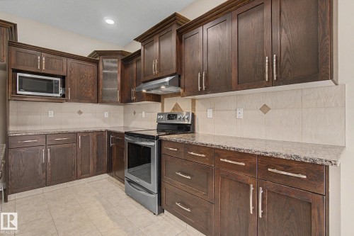 Kitchen featuring dark wood cabinetry, granite-finish countertops, and a tiled backsplash - 6016 10 Avenue Sw, Edmonton, AB - Indoor Photo Showing Kitchen