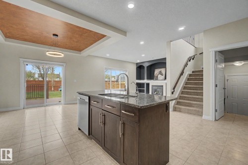 Open-concept living space featuring a central island with a granite countertop, a built-in fireplace with shelving, recessed lighting, and a coffered ceiling with a modern light fixture - 6016 10 Avenue Sw, Edmonton, AB - Indoor Photo Showing Kitchen With Upgraded Kitchen