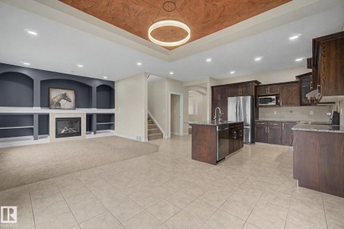 Kitchen and living area featuring a central island with sink, dark wood cabinetry, stainless steel appliances, and tile flooring - 6016 10 Avenue Sw, Edmonton, AB - Indoor Photo Showing Kitchen
