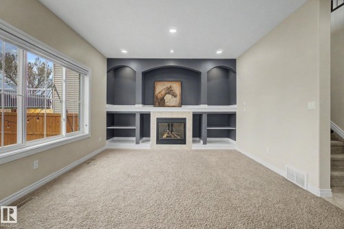Living area featuring a gas fireplace with a stone surround, built-in shelving with arched alcoves, recessed lighting, and a large multi-pane window - 6016 10 Avenue Sw, Edmonton, AB - Indoor With Fireplace