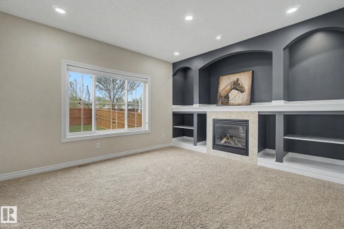 Living area featuring a gas fireplace with a tiled surround, built-in shelving, arched wall niches, recessed lighting, and carpet flooring - 6016 10 Avenue Sw, Edmonton, AB - Indoor With Fireplace