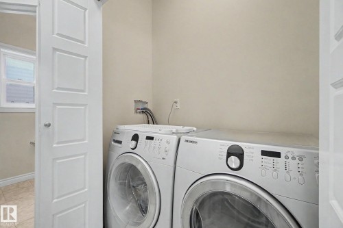 Dedicated laundry area featuring a front-loading washer and dryer, neutral wall paint, and a paneled door - 6016 10 Avenue Sw, Edmonton, AB - Indoor Photo Showing Laundry Room
