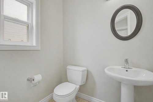 Compact bath featuring a white pedestal sink with chrome faucet, a white toilet, and a window with privacy glass - 6016 10 Avenue Sw, Edmonton, AB - Indoor Photo Showing Bathroom
