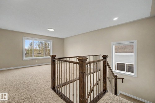 Carpeted open loft area featuring a dark wood and iron spindle railing, recessed lighting, and multiple windows with white trim - 6016 10 Avenue Sw, Edmonton, AB - Indoor Photo Showing Other Room