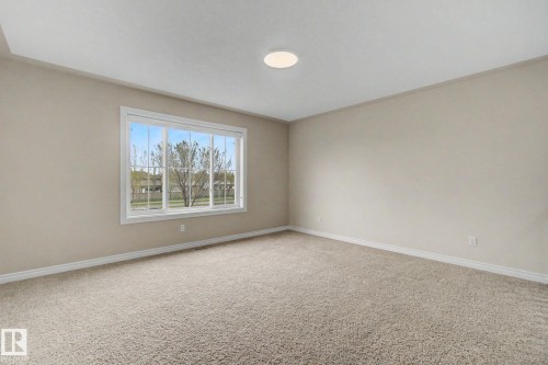 Light-filled room featuring a large multi-pane window with white trim, neutral wall color, and textured carpet flooring - 6016 10 Avenue Sw, Edmonton, AB - Indoor Photo Showing Other Room