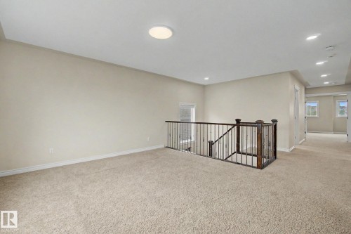 Spacious carpeted landing featuring a dark wood newel post and balusters, light neutral wall paint, and a flush mount ceiling light - 6016 10 Avenue Sw, Edmonton, AB - Indoor Photo Showing Other Room