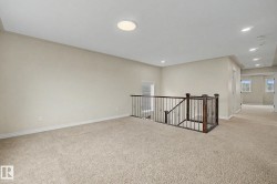 Spacious carpeted landing featuring a dark wood newel post and balusters, light neutral wall paint, and a flush mount ceiling light - 