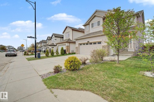 Two-story residence featuring light-toned siding, stone accents, and a double garage with horizontal paneling - 6016 10 Avenue Sw, Edmonton, AB - Outdoor