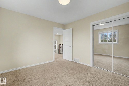 Neutral-toned carpeted room featuring a ceiling light fixture, white trim, and a mirrored sliding closet door - 6016 10 Avenue Sw, Edmonton, AB - Indoor Photo Showing Other Room