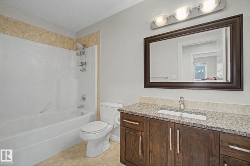 Bathroom featuring a spacious vanity with a light granite-style countertop, an undermount sink, and a dark wood-finish cabinet - 6016 10 Avenue Sw, Edmonton, AB - Indoor Photo Showing Bathroom