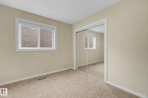 Bedroom featuring neutral carpeting, a dual-pane window with white trim, and a full-height mirrored closet - 6016 10 Avenue Sw, Edmonton, AB - Indoor Photo Showing Other Room