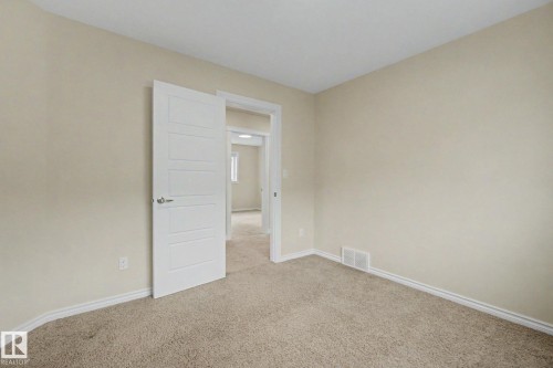 Light-toned carpeting and walls create a neutral palette, complemented by white trim and a contemporary five-panel interior door - 6016 10 Avenue Sw, Edmonton, AB - Indoor Photo Showing Other Room