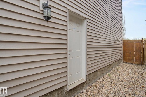 Exterior featuring beige horizontal siding, a white entry door, an exterior wall light, a wooden fence, and a gravel ground cover - 6016 10 Avenue Sw, Edmonton, AB - Outdoor