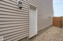 Exterior featuring beige horizontal siding, a white entry door, an exterior wall light, a wooden fence, and a gravel ground cover - 