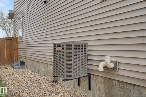 Exterior wall with tan horizontal siding, a visible air conditioning unit, foundation with textured finish, and a window well with a corrugated metal surround - 6016 10 Avenue Sw, Edmonton, AB - Outdoor