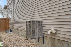 Exterior wall with tan horizontal siding, a visible air conditioning unit, foundation with textured finish, and a window well with a corrugated metal surround - 