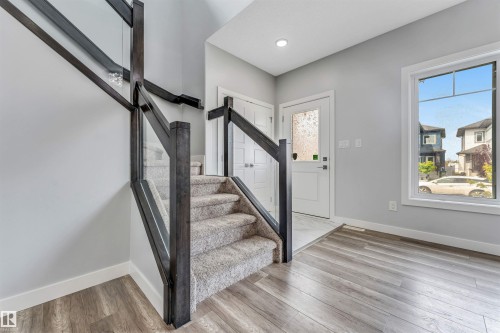 Modern entryway featuring a carpeted staircase with glass and dark wood railings, wood-finish flooring, and a white front door with decorative glass - 6075 180 Avenue Nw, Edmonton, AB - Indoor Photo Showing Other Room