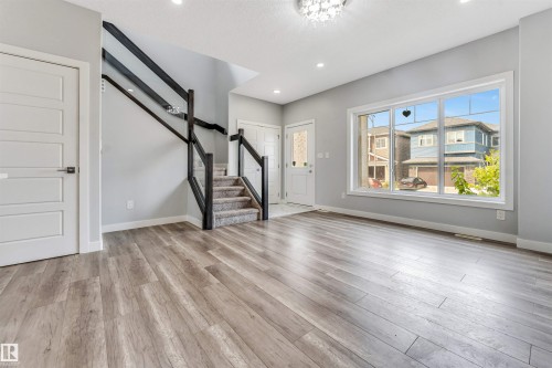 Open-concept living space featuring wood-finish flooring, a large multi-pane window, and a carpeted staircase with a dark wood railing - 6075 180 Avenue Nw, Edmonton, AB - Indoor Photo Showing Other Room