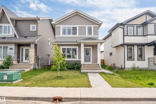 Contemporary two-story residence featuring a gray and beige siding exterior, a front porch with white columns, concrete steps, and a white front railing - 6075 180 Avenue Nw, Edmonton, AB - Outdoor With Facade