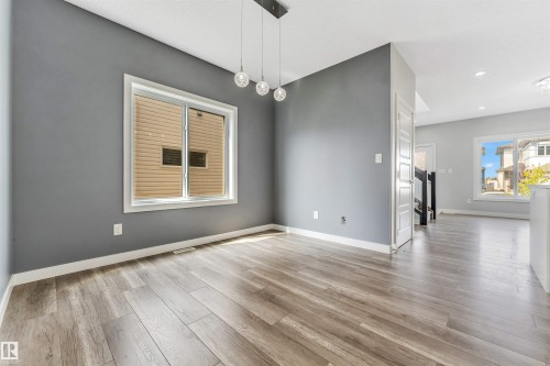 Open-concept living space featuring wood-finish flooring, a contemporary pendant light fixture, and a large window with white trim - 6075 180 Avenue Nw, Edmonton, AB - Indoor Photo Showing Other Room