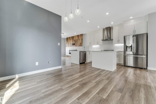 Open-concept living space featuring wood-finish flooring, a modern kitchen with white cabinetry, stainless steel appliances, a white subway tile backsplash, and a central island - 6075 180 Avenue Nw, Edmonton, AB - Indoor Photo Showing Kitchen With Stainless Steel Kitchen With Upgraded Kitchen