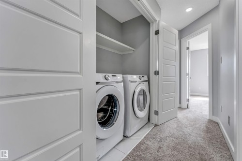 Dedicated laundry closet featuring a front-load washer and dryer, built-in shelving, white tile flooring, and a paneled bifold door - 6075 180 Avenue Nw, Edmonton, AB - Indoor Photo Showing Laundry Room