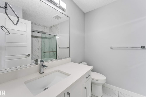 Bathroom featuring a white vanity with an integrated sink and chrome faucet, a large frameless mirror, and overhead linear lighting - 6075 180 Avenue Nw, Edmonton, AB - Indoor Photo Showing Bathroom