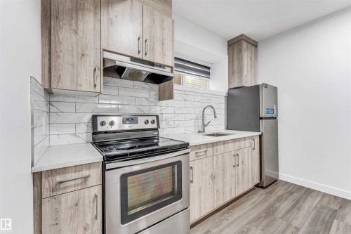 Kitchen featuring wood-finish cabinetry with silver hardware, white countertops, and a subway tile backsplash - 6075 180 Avenue Nw, Edmonton, AB - Indoor Photo Showing Kitchen With Stainless Steel Kitchen With Upgraded Kitchen