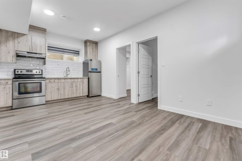 Contemporary kitchen featuring wood-finish cabinetry, stainless steel appliances, white subway tile backsplash, and light wood-finish flooring - 6075 180 Avenue Nw, Edmonton, AB - Indoor Photo Showing Kitchen With Stainless Steel Kitchen
