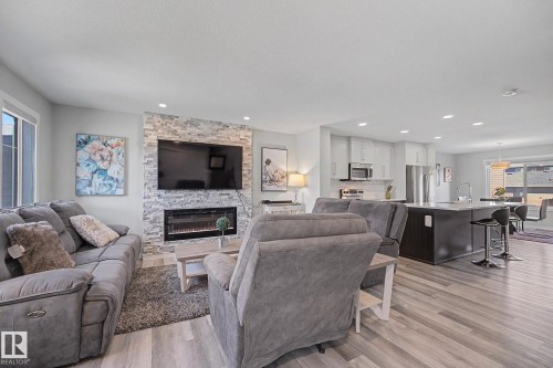 Living area featuring wood-finish flooring, a stacked stone fireplace surround with an electric insert, recessed lighting, and an open concept layout - 2314 Wonnacott Crescent Sw, Edmonton, AB - Indoor Photo Showing Living Room With Fireplace
