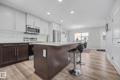 Modern kitchen featuring two-tone cabinetry with white upper cabinets and dark wood-finish lower cabinets, stainless steel appliances, and a subway tile backsplash - 2314 Wonnacott Crescent Sw, Edmonton, AB - Indoor Photo Showing Kitchen With Upgraded Kitchen