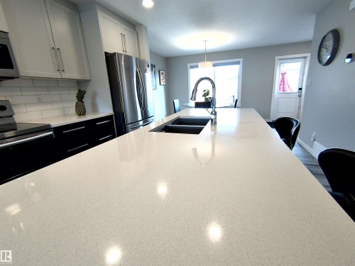 Spacious kitchen island featuring a dual-basin undermount sink with a gooseneck faucet, light-toned countertop, and bar seating - 2314 Wonnacott Crescent Sw, Edmonton, AB - Indoor Photo Showing Kitchen With Double Sink With Upgraded Kitchen