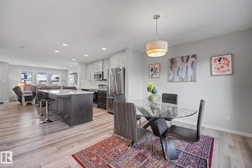 Open-concept kitchen and dining area featuring stainless steel appliances, a large center island with seating, wood-finish flooring throughout, and abundant natural light from multiple windows - 2314 Wonnacott Crescent Sw, Edmonton, AB - Indoor Photo Showing Dining Room