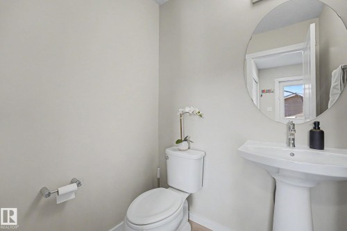 Contemporary powder room featuring a pedestal sink, round mirror, chrome-finish faucet, and light neutral wall tones - 2314 Wonnacott Crescent Sw, Edmonton, AB - Indoor Photo Showing Bathroom