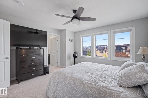Carpeted room featuring a ceiling fan with integrated lighting, a wall-mounted television, and a three-pane window offering exterior views - 2314 Wonnacott Crescent Sw, Edmonton, AB - Indoor Photo Showing Bedroom