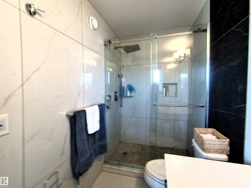 Glass-enclosed shower with a pebble-tiled floor, rain shower head, and built-in shower niche - 2314 Wonnacott Crescent Sw, Edmonton, AB - Indoor Photo Showing Bathroom