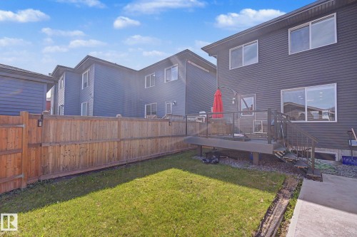 Private backyard featuring a wooden fence with integrated lighting, a spacious dark composite deck with glass railings, and stairs providing access to the grassy area - 2314 Wonnacott Crescent Sw, Edmonton, AB - Outdoor With Deck Patio Veranda