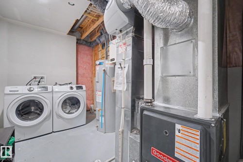 Dedicated laundry area featuring a front-loading washer and dryer, adjacent to mechanical systems including a water heater and furnace - 2314 Wonnacott Crescent Sw, Edmonton, AB - Indoor Photo Showing Laundry Room
