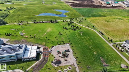 Aerial perspective showcasing extensive green spaces, a contemporary building with solar panels, and a dedicated playground area - 2314 Wonnacott Crescent Sw, Edmonton, AB - Outdoor With View