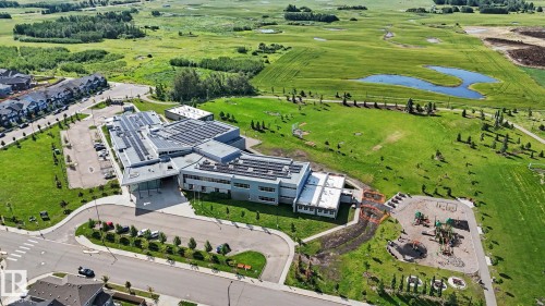 Modern institutional building with solar panels, extensive green space, adjacent playground, and nearby residential development - 2314 Wonnacott Crescent Sw, Edmonton, AB - Outdoor With View