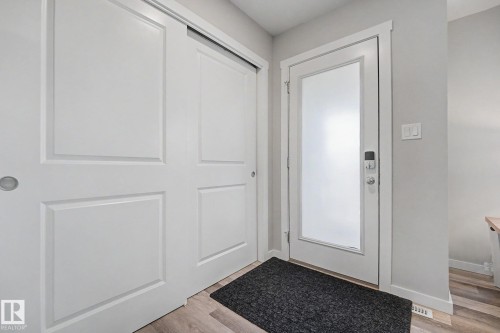 Entryway featuring a white frosted glass door, adjacent sliding panel closet doors, light wood-finish flooring, and light gray wall paint - 2314 Wonnacott Crescent Sw, Edmonton, AB - Indoor Photo Showing Other Room