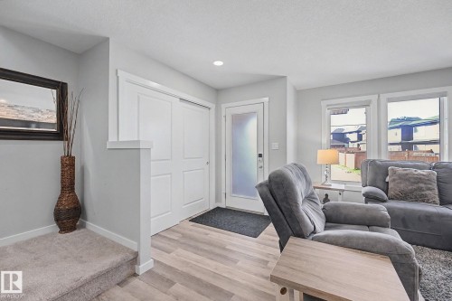 Entryway featuring wood-finish flooring, a contemporary frosted glass front door, and a built-in closet with sliding panel doors - 2314 Wonnacott Crescent Sw, Edmonton, AB - Indoor Photo Showing Living Room