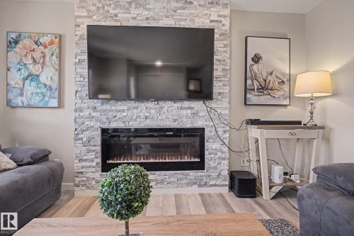 Living area featuring a stone accent wall with an integrated electric fireplace and a mounted television - 2314 Wonnacott Crescent Sw, Edmonton, AB - Indoor Photo Showing Living Room With Fireplace