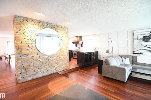 The stacked stone feature wall also incorporates a gas fireplace on the kitchen and dining room side, and adds charm and warmth.  Brazilian Tigerwood flooring throughout the main floor ties both the social, and private family spaces together - 572 Lessard Drive Nw, Edmonton, AB - Indoor Photo Showing Living Room
