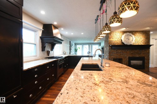 9 pendant lights over the 13 foot island, pot lights in the ceiling, a gas fireplace, and a wet par area with glass cabinet doors.  Details matter - 572 Lessard Drive Nw, Edmonton, AB - Indoor Photo Showing Kitchen With Double Sink