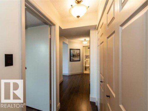 Hallway featuring dark wood-finish flooring, white walls, and paneled closet doors with black hardware - #1203 10025 113 St Nw, Edmonton, AB - Indoor Photo Showing Other Room