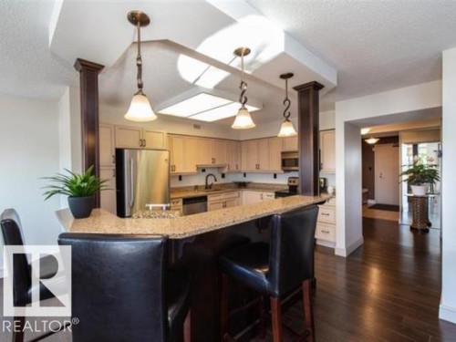 Kitchen featuring a breakfast bar with stone countertop, stainless steel appliances, wood-finish flooring, recessed lighting, and pendant light fixtures - #1203 10025 113 St Nw, Edmonton, AB - Indoor Photo Showing Kitchen With Upgraded Kitchen
