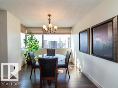 Dining area featuring expansive windows, wood-finish flooring, a classic chandelier, and white baseboards - #1203 10025 113 St Nw, Edmonton, AB - Indoor Photo Showing Dining Room