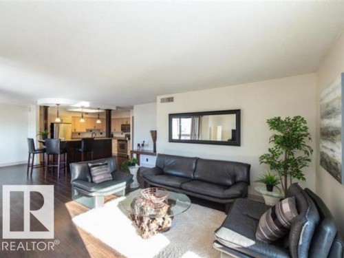 Open-concept living area with dark wood-finish flooring, a kitchen featuring stainless steel appliances, and a breakfast bar with pendant lighting - #1203 10025 113 St Nw, Edmonton, AB - Indoor Photo Showing Living Room