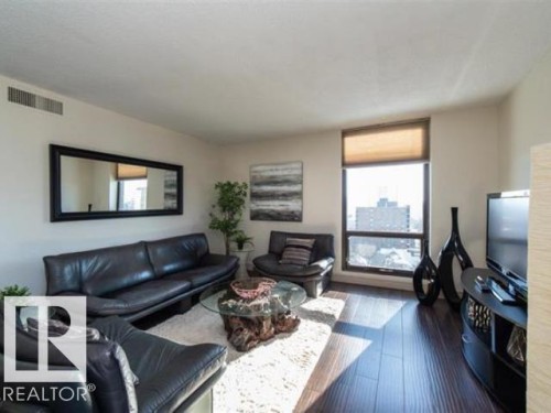 Living space featuring dark wood-finish flooring and a large window with roller shade - #1203 10025 113 St Nw, Edmonton, AB - Indoor Photo Showing Living Room